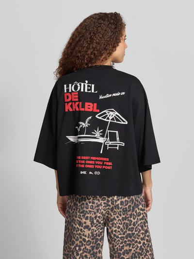 Frauenmodel trägt Cropped T-Shirt mit Statement-Print Modell 'Vacation' von Karo Kauer, schwarze Reine Baumwolle, Oversized-Fit, Ganzkörperansicht Rückansicht.