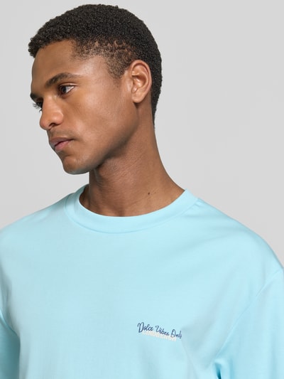 Männermodel trägt Oversized T-Shirt mit Label-Print von Lindbergh in Hellblau aus Reine Baumwolle, Rundhalsausschnitt, Nahaufnahme Oberkörper.