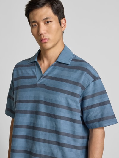 Männermodel trägt Oversized Poloshirt mit Logo-Patch von MAISON KITSUNÉ aus reiner Baumwolle, Oversized-Fit, blau gestreift, Nahaufnahme Oberkörper.