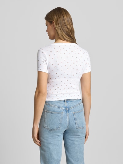 Vrouwenmodel draagt Cropped T-shirt met V-hals en knoopsluiting van Guess Jeans, materiaalmix met viscose, kort, logoprint, ruglengte maat S 43 cm. Ganzekijk rugaanzicht.