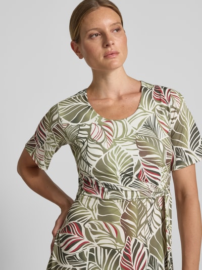 Frauenmodel trägt Knielanges Kleid im Allover-Look mit Rundhalsausschnitt von MORE & MORE, grün-weißes Blattmuster, Nahaufnahme Oberkörper. Material-Mix mit Stretch-Anteil, A-Linie, knielang, Rückenlänge 99 cm, Brustweite 42 cm, Ärmellänge 26 cm.