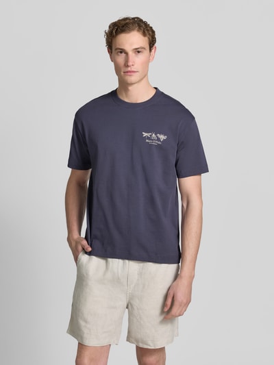 Męski model nosi Relaxed Fit T-Shirt aus reiner Baumwolle von Marc O'Polo, jednokolorowy dżersej, krój regular fit, nadruk z logo, okrągły dekolt, krótki rękaw, bawełna, całkowity widok z przodu.