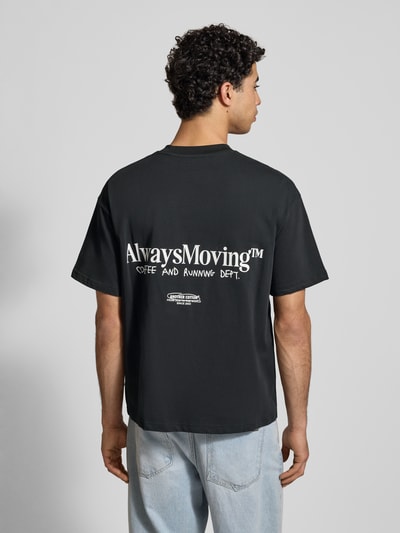 Männermodel trägt T-Shirt mit Label-Print von ANOTHER COTTON LAB aus reiner Baumwolle im lockeren Schnitt, Rückenansicht, Rückenlänge 71 cm bei Größe M.