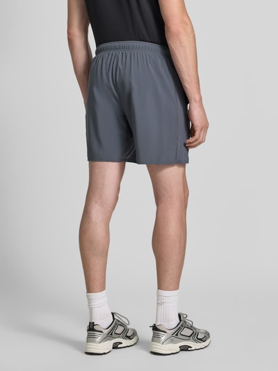 Mężczyzna nosi Regular Fit Shorts mit integriertem Slip Modell 'Core' od ASICS TIGER w kolorze szarym, elastyczny pas, nadruk z logo, szerokość w rozmiarze M: 38 cm, długość wewnętrzna nogawki: 17 cm, całkowity widok z tyłu.
