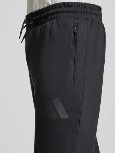 Männermodel trägt Sweatpants mit Logo und elastischem Bund von adidas Sportswear, Materiaalmix met katoen, regular fit, logoprint, elastische band, tunnelkoord, binnenbeenlengte maat M 75 cm. Detailaufnahme rechter heup.