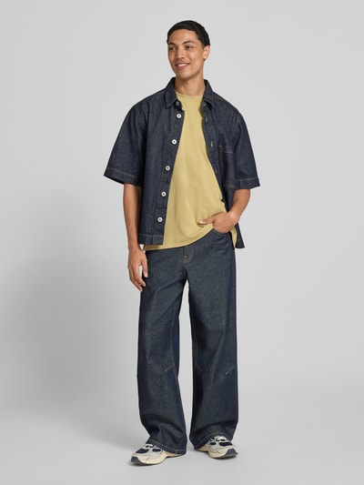 Männermodel trägt Relaxed Fit T-Shirt aus reiner Baumwolle von Marc O'Polo Denim in Gelb zu dunkler Jeans, Herren T-Shirt, Ganzkörperansicht von vorne.