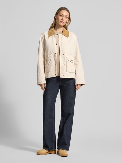 Vrouwenmodel draagt Jacke mit Umlegekragen und aufgesetzten Pattentaschen van WHITE LABEL in recht model met platte kraag, drukknoopsluiting, opgestikte klepzakken, ruglengte maat 36: 67 cm, schouderbreedte: 44 cm, borstwijdte: 53 cm, mouwlengte: 63 cm, lichte crèmekleuren, gladde textuur, donkere broek, bruine schoenen. Volledig frontaal totaalbeeld.