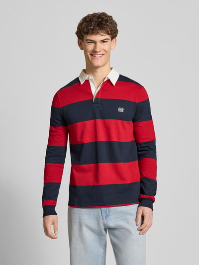 Männermodel trägt Regular Fit Poloshirt mit Rugby-Streifen und Logo-Bestickung von REVIEW in Rot und Dunkelblau, reine Baumwolle, Nahaufnahme Oberkörper.