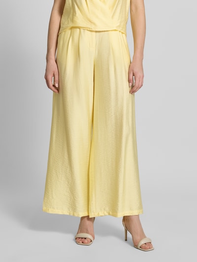 Vrouwenmodel draagt Wide Leg Pants aus Viskose-Mix mit Eingrifftaschen van GUIDO MARIA KRETSCHMER WOMAN, lichtgeel, uitlopend model, Franse steekzakken, knoop- en ritssluiting, model 'Finja', gladde textuur, lichte glans, detailopname onderlichaam.