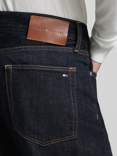 Männermodel trägt Straight Fit Jeans aus reiner Baumwolle von Tommy Hilfiger, dunkle Denimoptik, Label Patch, Nahaufnahme Rückansicht.