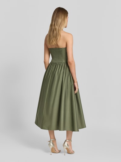 Modelka kobieca nosi 'Cocktailkleid im Off-Shoulder-Look mit Smok-Details' od Jake*s Cocktail, mieszanka bawełny i elastanu, linia a, sukienka midi, odkryte ramiona, marszczone detale, długość tyłu w rozmiarze 36: 104 cm, szerokość w rozmiarze 36: 35 cm, jednolity khaki, gładka tekstura, widok całej sylwetki z tyłu.