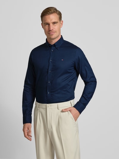 Męski model nosi Regular Fit Businesshemd aus reiner Baumwolle od Tommy Hilfiger w kolorze granatowym, z długim rękawem i logo, zdjęcie całej sylwetki z przodu.
