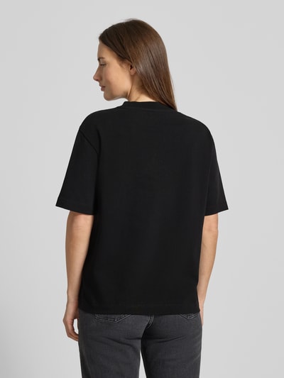 Frauenmodel trägt T-Shirt mit Label-Stitching Modell 'TARJAA' von ARMEDANGELS aus schwarzer Bio-Baumwolle, lockerer Schnitt, Ganzkörperansicht Rückansicht.