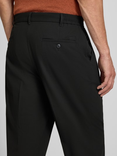 Mężczyznamodel nosi Straight Fit Hose mit Viskose-Anteil von MCNEAL, czarny, elastyczna mieszanka materiałów z dodatkiem wiskozy, zakładki w pasie, kieszenie z tyłu, zapięcie na guzik i zamek błyskawiczny, szerokość w rozmiarze M: 41 cm, długość wewnętrzna nogawki w rozmiarze M: 75 cm. Detailaufnahme tyłu.