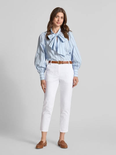 Kobiece model prezentuje Chino mit Fransensaum von Marc Cain, mieszanka bawełny z dodatkiem streczu, krój slim fit, zapięcie na guzik i zamek błyskawiczny, wpuszczane kieszenie z przodu, frędzle na dole, kieszenie z tyłu, szerokość w rozmiarze 36: 40 cm, długość wewnętrzna nogawki w rozmiarze 36: 67 cm, widok całej sylwetki z przodu.