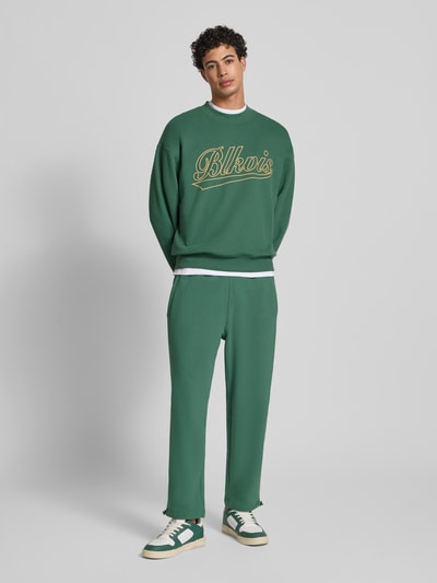Męski model nosi Regular Fit Sweatpants mit Gesäßtasche Modell 'Source' od BLKVIS, czysta bawełna, kieszeń z tyłu, elastyczny pas, długość 7/8, krój regular fit, zielony kolor, widok całej sylwetki z przodu.