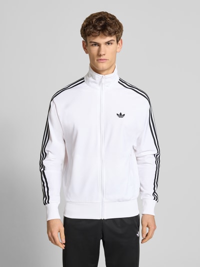 Männermodel trägt Trainingsjacke mit Stehkragen von adidas Originals in Weiß mit schwarzen Streifen, Regular Fit, Ganzkörperansicht von vorne.