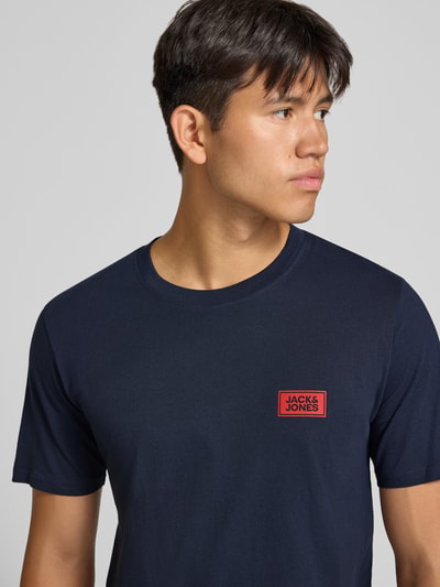 Männermodel trägt Regular Fit T-Shirt aus reiner Baumwolle mit Label-Detail von JACK & JONES, dunkelblau, Nahaufnahme Oberkörper. Rückenlänge bei Größe M: 67 cm, Rundhalsausschnitt, glatte Textur.