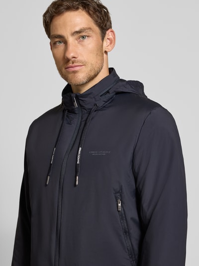Männermodel trägt Regular Fit Bomberjacke mit Logo-Detail von Armani Exchange in Dunkelblau, glatte Struktur, Nahaufnahme Oberkörper, elastischer Material-Mix, Zweiwege-Reißverschluss, Stehkragen mit Tunnelzug, Eingrifftaschen.