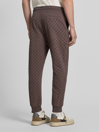 Männermodel trägt braune Herren Sweathose mit Allover-Logomuster von JOOP! COLLECTION, weiche Textur, Ganzkörperansicht Rückansicht.