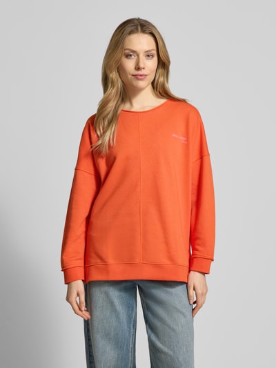 Modelka nosi Oversized Sweatshirt mit Label-Print od Smith and Soul, kolor pomarańczowy, bawełniano-modalowy mix, długie rękawy, okrągły dekolt, ściągacze, nadruk z logo, widok całej sylwetki z przodu.