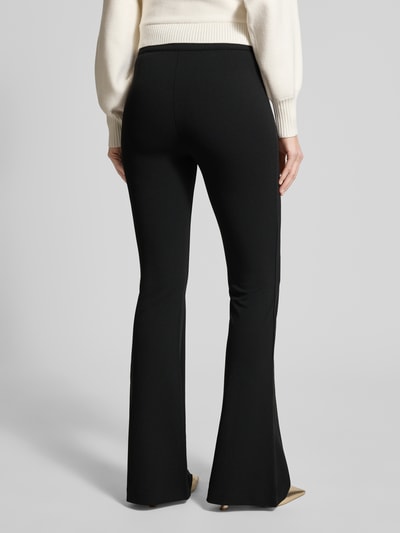 Frauenmodel trägt schwarze Flared Fit Stoffhose mit elastischem Bund Modell 'Evelina' von Guess, Ziernähte, Ganzkörperansicht Rückansicht.