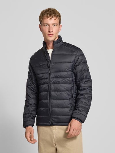 Męski model nosi Regular Fit kurtkę z efektem pikowania Model 'Kingsley' od JACK & JONES, kolor czarny, stójka, zamek błyskawiczny, wpuszczane kieszenie, całkowity widok z przodu, długość tyłu w rozmiarze M: 72 cm, szerokość ramion w rozmiarze M: 48 cm, szerokość w rozmiarze M: 51 cm, długość rękawów w rozmiarze M: 68 cm.