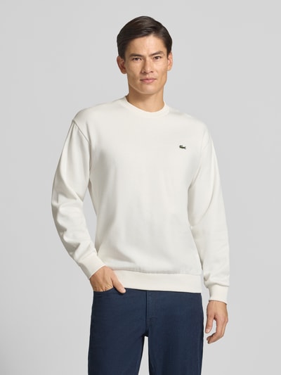 Männermodel trägt ein weißes Regular Fit Sweatshirt aus Baumwoll-Mix von Lacoste, kombiniert mit dunkelblauer Hose, Ganzkörperansicht von vorne. Herren Sweatshirt von Lacoste.