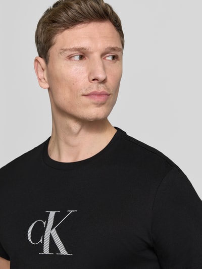 Männermodel trägt T-Shirt mit Rundhalsausschnitt und Logo von CK Calvin Klein, reine Baumwolle, Regular Fit, schwarze Farbe, Nahaufnahme Oberkörper