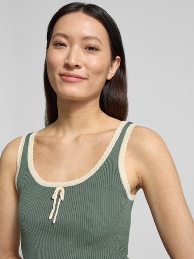 Frauenmodel trägt Slim Fit Tank Top aus Viskose-Mix Modell 'Bardot' von Vero Moda in Optik: Unifarben, Rippstrick, U-Ausschnitt, breite Träger, grün mit beigen Details, Materialverarbeitung: Viskose-Mix, Nahaufnahme Oberkörper.