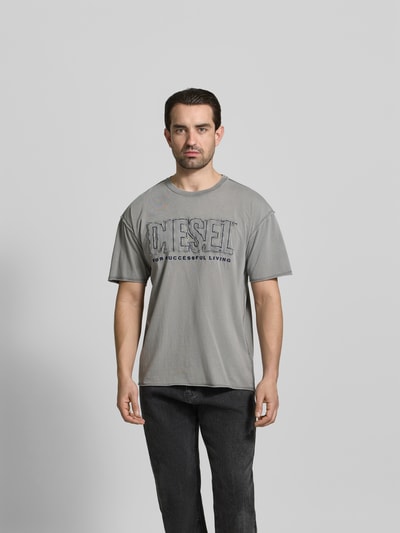 Männermodel trägt Regular Fit T-Shirt mit Logo-Detail von Diesel, Herren T-Shirt aus reiner Baumwolle, Rundhalsausschnitt, Kurzärmelig, Logo-Detail, graue Farbe, Rückenlänge bei Größe M 76 cm, Ganzkörperansicht von vorne.