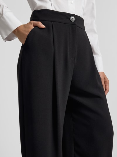 Frauenmodel trägt Relaxed Fit Hose mit Bundfalten von ARMANI EXCHANGE in Schwarz mit Eingrifftaschen, Nahaufnahme Oberkörper.