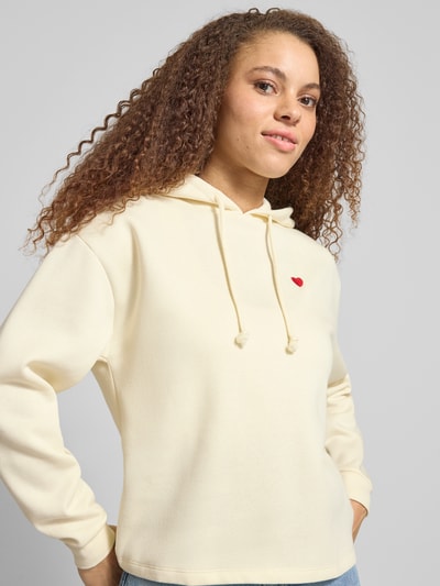 Modelka nosi Regular Fit Hoodie aus Baumwoll-Mix Modell 'CHILLI' od Pieces w kolorze jednolitym, haft, długie rękawy, bluza z kapturem, dzianina dresowa; zbliżenie na górną część ciała.