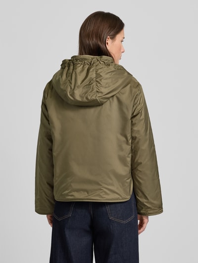 Modelka kobieca nosi Relaxed Fit Funktionsjacke mit Woll-Füllung Modell 'AGRESTE' od Weekend Max Mara w jednolitym, oliwkowym kolorze, z kapturem i bocznymi kieszeniami, wodoodporna, z logo, widok całej sylwetki od tyłu.