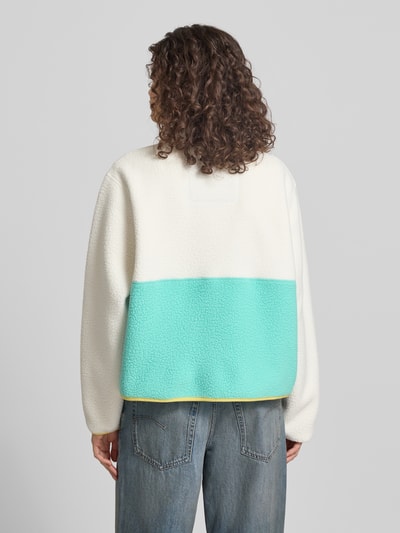 Frauenmodel trägt Fleecejacke mit Brusttasche und Label-Patch von Superdry in Creme und Türkis, Gerader-Schnitt, Stehkragen, Ganzkörperansicht Rückansicht, Rückenlänge 57 cm, Schulterbreite 49 cm, Brustweite 61 cm, Ärmellänge 62 cm