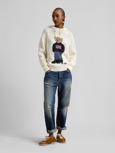 Frauenmodel trägt Comfort Fit Strick-Hoodie mit Polo-Bear-Intarsia von Polo Ralph Lauren in Creme, Leinen-Baumwoll-Mix, unifarben, gerippte Abschlüsse, Kapuze, lange Ärmel, Ganzkörperansicht von vorne.