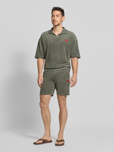 Männermodel trägt Regular Fit Sweatshorts aus Baumwoll-Mix Modell 'TERRANCE' von HUGO in Olivgrün mit Label Patch und seitlichen Eingrifftaschen, Ganzkörperansicht von vorne.