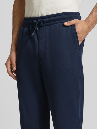 Männermodel trägt dunkelblaue Sweatpants mit Baumwoll-Anteil Modell 'KANE BRADLEY' von JACK & JONES, Nahaufnahme Oberkörper, Material-Mix, Gerade Passform, elastischer Bund mit Tunnelzug, Eingrifftaschen, Herren, Innenbeinlänge bei Größe M 71 cm.