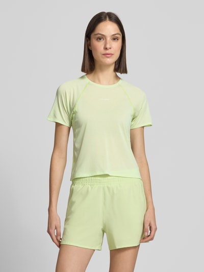 Frauenmodel trägt Cropped T-Shirt mit Rundhalsausschnitt Modell 'SHKOUT' von Salomon in zartem Pastellgrün mit Raglanärmeln, taillierte Passform, Nahaufnahme Oberkörper.