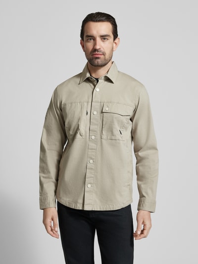 Męski model nosi Regular Fit Hemdjacke mit Brusttaschen od camel active, bawełniany miks ze stretchem, jasnobeżowy kolor, prosty krój, kołnierzyk kent, guziki, kieszenie na piersi, długość tyłu w rozmiarze M 74 cm, szerokość ramion w rozmiarze M 47 cm, szerokość w rozmiarze M 58 cm, długość rękawa w rozmiarze M 66 cm, widok całej sylwetki z przodu.
