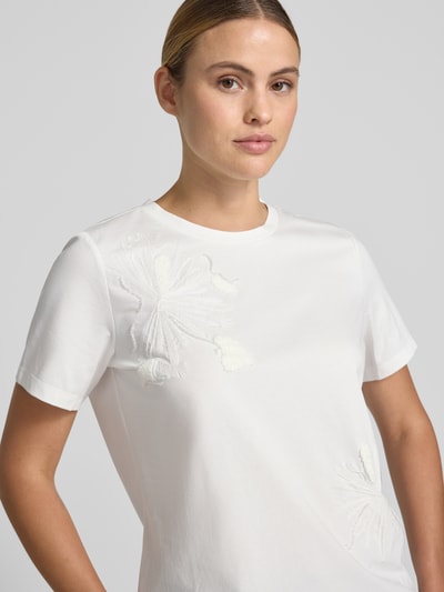 Modelka kobieca nosi T-Shirt mit Stitchings und Rundhalsausschnitt von Jake*s Collection, bawełniany miks, krój regular fit, detal haftu, kolor biały, długość tyłu w rozmiarze S: 56 cm, zbliżenie na górną część ciała