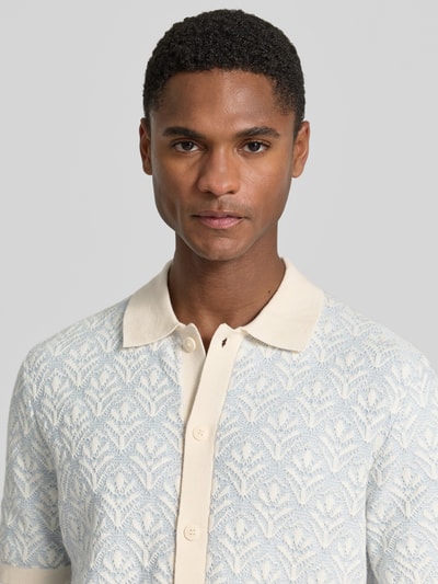 Männermodel trägt Strickshirt mit Polokragen und durchgehender Knopfleiste von MCNEAL, cremefarbene Knopfleiste, Allover-Muster, Nahaufnahme Oberkörper.