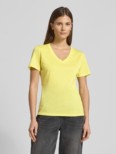 Frauenmodel trägt Regular Fit T-Shirt aus Viskose-Mix von LIU JO SPORT in Gelb mit Glitzer-Optik und Logo-Detail, Nahaufnahme Oberkörper.