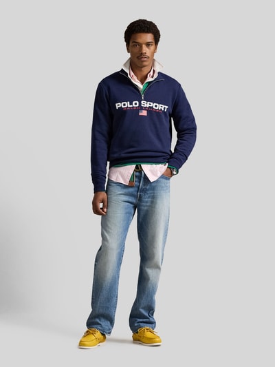 Männermodel trägt Relaxed Fit Troyer aus Baumwoll-Mix von Polo Ralph Lauren, dunkelblauer Sweatstoff, Label Print, Ganzkörperansicht von vorne.