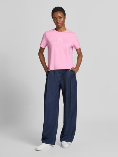 Vrouwenmodel draagt Boxy Fit t-shirt uit pure katoen model 'SARA' van VERO MODA in lichtroze met donkerblauwe broek, Ganzlichaamsaanzicht van voren.