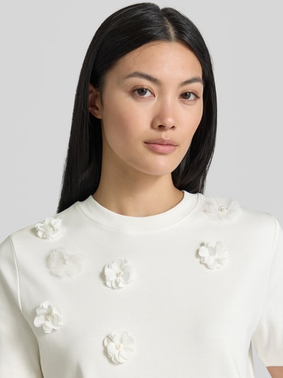 Frauenmodel trägt T-Shirt mit floralen Applikationen von Christian Berg Woman, Reine Baumwolle, gerader-Schnitt, Rundhalsausschnitt, 1/2-Arm, Nahaufnahme Oberkörper.