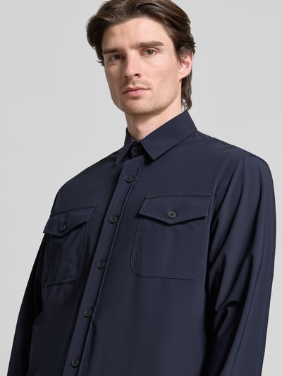 Männermodel trägt Hemdjacke mit Knopfleiste von CRUNA in Dunkelblau, Kentkragen, Brusttaschen, Material-Mix, Nahaufnahme Oberkörper.