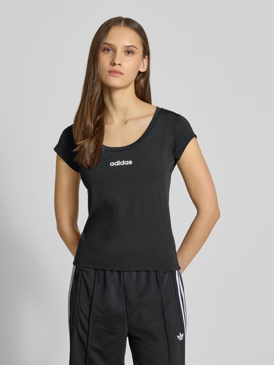 Frauenmodel trägt Cropped T-Shirt mit Label-Print von adidas Sportswear in Schwarz, Material-Mix mit Stretch-Anteil, Slim Fit, gerippter Rundhalsausschnitt, Rückenlänge bei Größe S 49 cm, Label-Print vorne, Ganzkörperansicht von vorne.