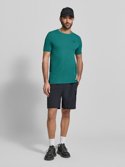 Männermodel trägt Slim Fit T-Shirt mit Logo-Print Modell 'Vanish' von Under Armour in Türkis mit Lochmuster, Ganzkörperansicht von vorne.