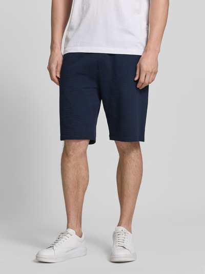 Mężczyzna nosi Relaxed Fit Bermudas aus Baumwoll-Mix Modell 'DETROIT' od s.Oliver RED LABEL, granatowy kolor, struktura waflowa, elastyczny pas z troczkiem, bawełniany materiał, widok przód, ujęcie całej sylwetki